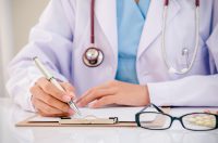 doctor writing record on folder while holding medicine in office